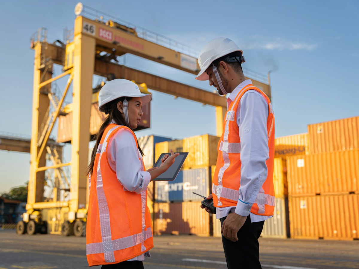 Two workers in hard hats reviewing plans in a container yard